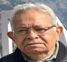 Close-up view of a person's head with short, light-colored hair. Their face is not visible, and the background features a textured wall with muted tones.